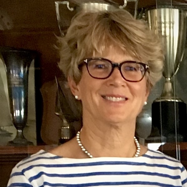 A portrait-style photo of a smiling person wearing glasses and a striped shirt, with trophies and glassware in the background. No readable text is visible.